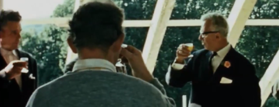 Billede fra filmen, der viser nogle herrer, der skåler med hinanden ved et rejsegilde.